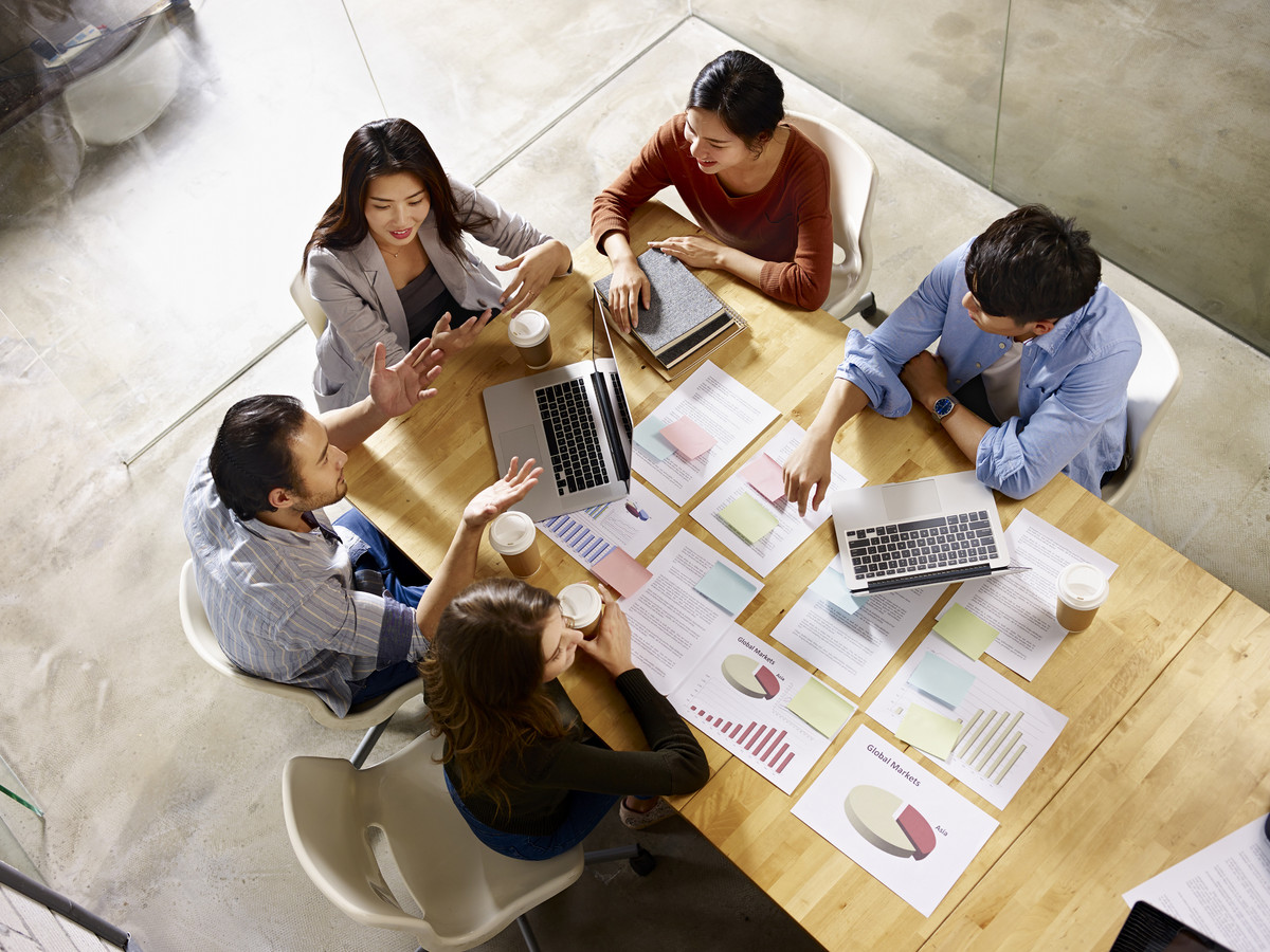 Ein Business Team sitz an einem Tisch mit vielen Business Charts und diskutiert