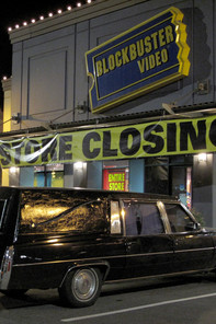 a hearse parking in front of a closed Blockbuster Videos store