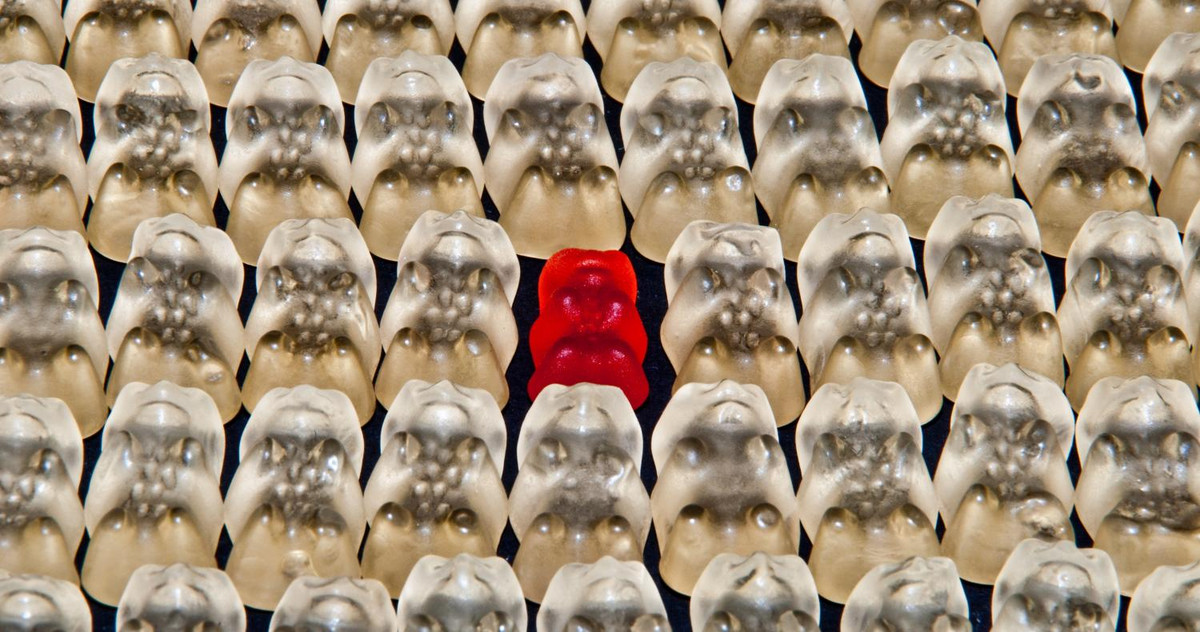 Picture of a red jelly bear, standing out of a white crowd