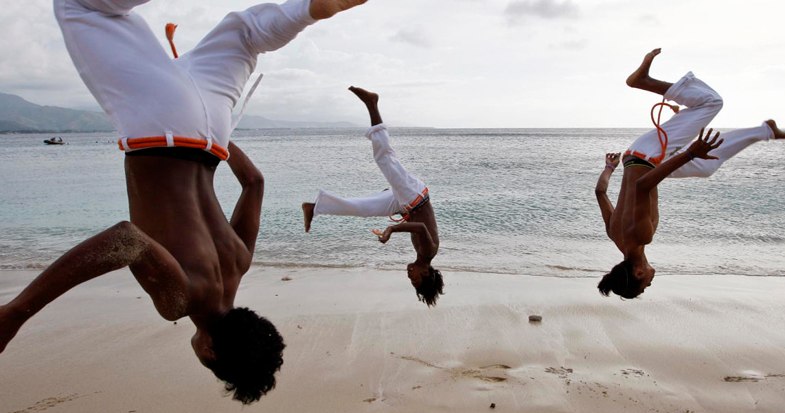 Drei Männer beim Capoeira auf dem Strand, das Meer im Hintergrund