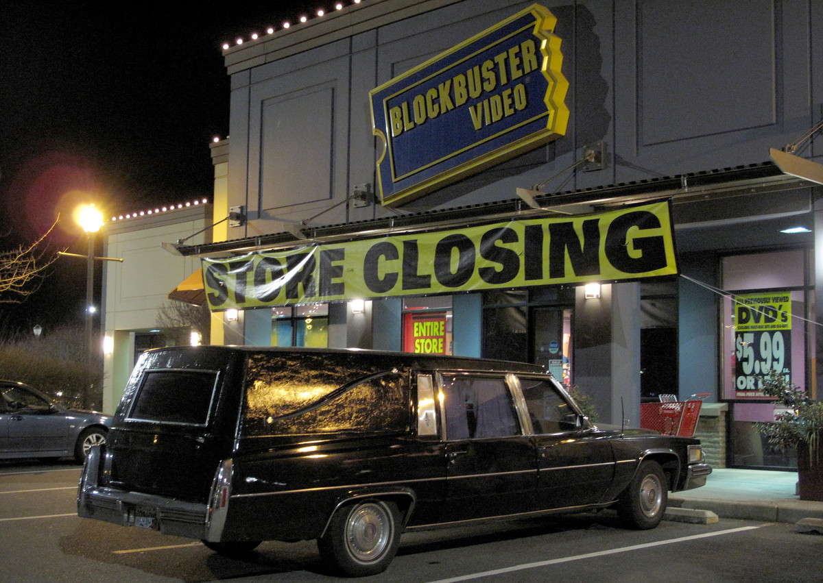 a hearse parking in front of a closed Blockbuster Videos store