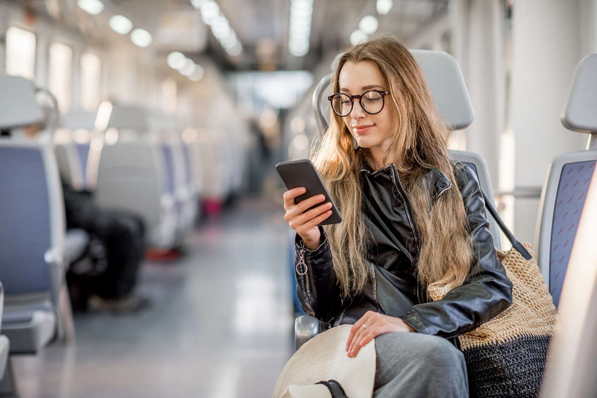 Eine junge Frau in einem Zugwagon sitzend schaut auf ihr Mobiltelefon