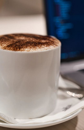 Eine Kaffeetasse mit Kaffee darin neben einem Laptop mit Geschäftszahlen darauf