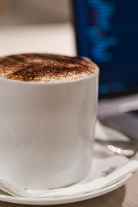 Eine Kaffeetasse mit Kaffee darin neben einem Laptop mit Geschäftszahlen darauf