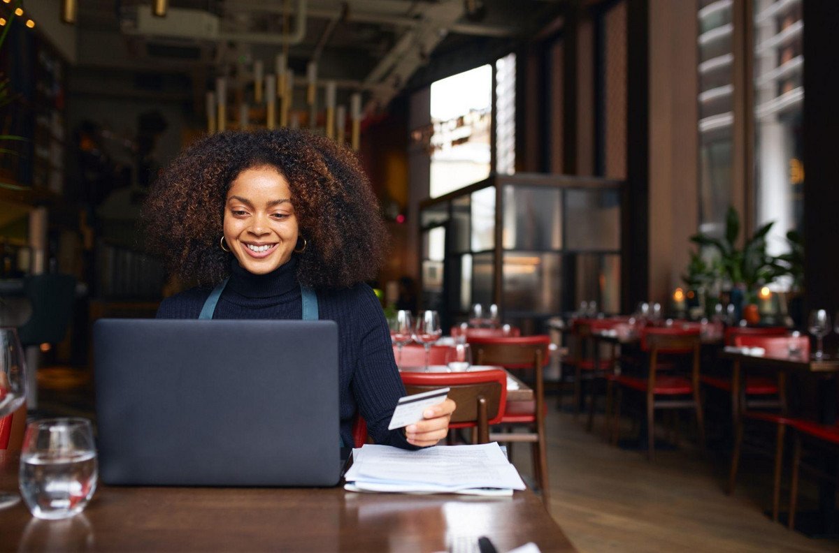 A woman in front of a laptop with her credit card in her hand
