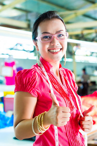 Asian dressmaker in a textile factory showing thumbs up