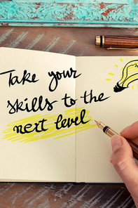 Jemand schreibt in sein Notizbuch über 2 Seiten erstreckend "Take your skills to the next level"