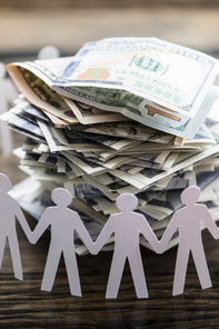 A pile of banknotes, surrounded by cut out, holding hands paper men