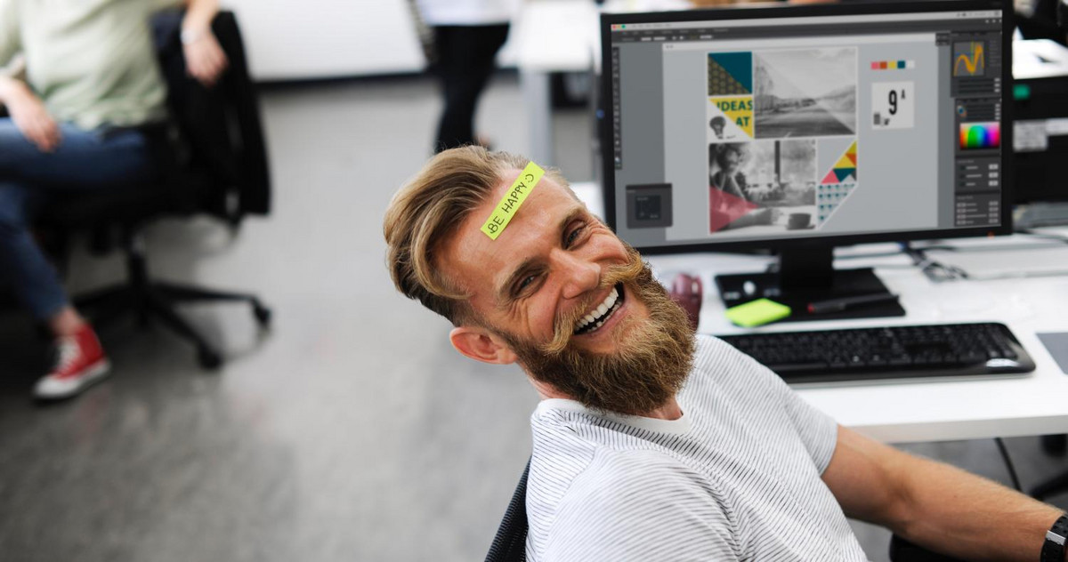 Bild eines lachenden Mitarbeiters an seinem Arbeitsplatz