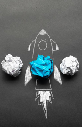 Several white paper balls, inside a blue one, around which a rocket taking off is painted with chalk 