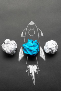 Several white paper balls, inside a blue one, around which a rocket taking off is painted with chalk 