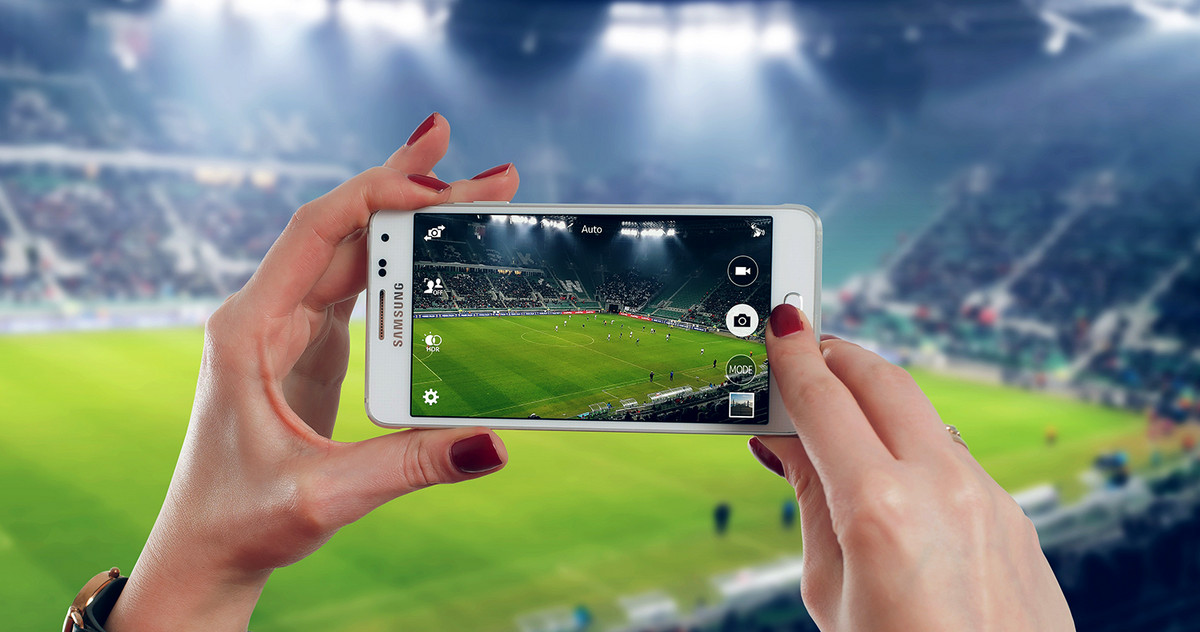 A woman is making a picture of a soccer field with her phone