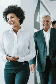 A young business woman smiling and an older business man standing behind her