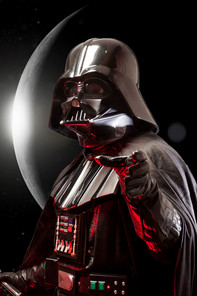 Darth Vader stands in front of the moon with a red laser sword