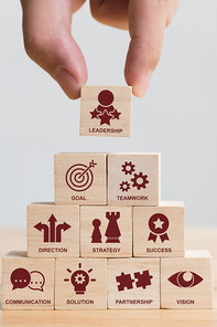 Wooden blocks, with symbols for leadership themes on them, are stacked by one hand to form a pyramid
