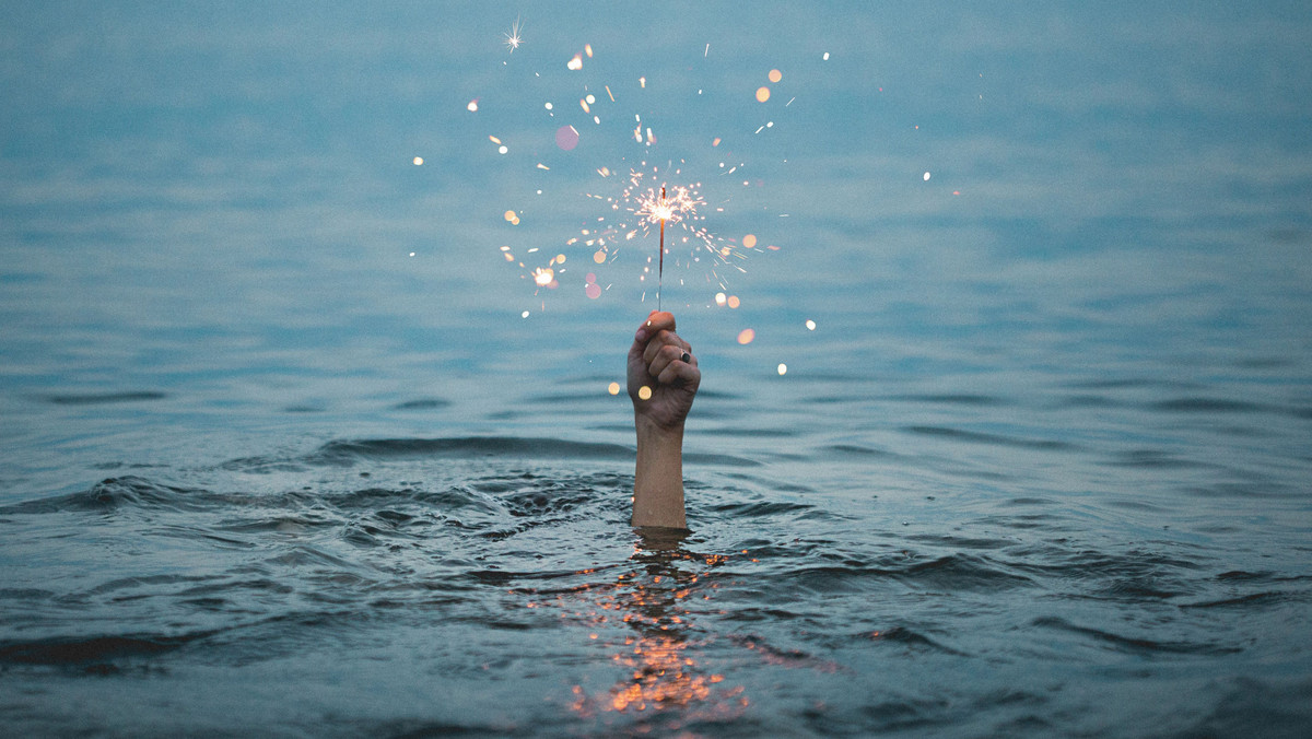 A hand is holding a sparkler over water