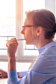 A woman is thinking about something and holding a pen to her mouth