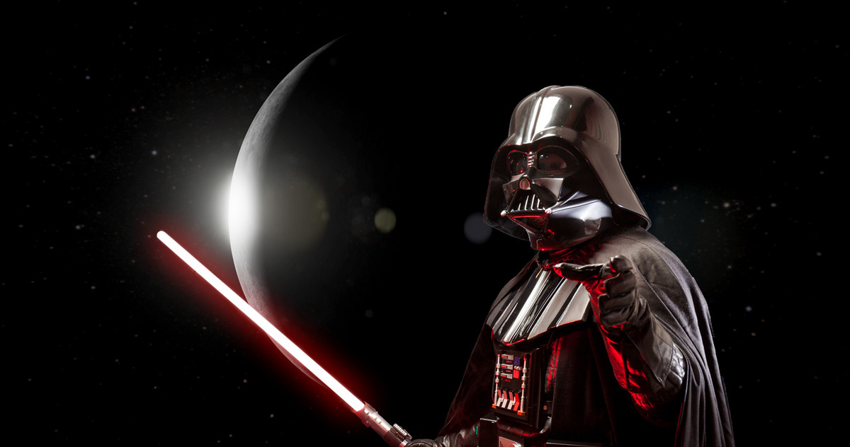 Darth Vader stands in front of the moon with a red laser sword