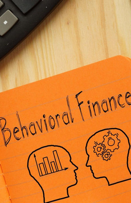 Ein Taschenrechner und ein Notizblock in dem "Behavioral Finance" notiert steht, darunter eine Zeichnung von zwei Köpfen