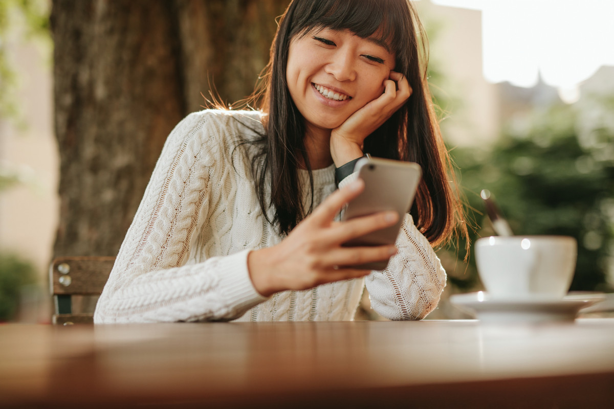 Happy young woman looking at her smartphone outdoors