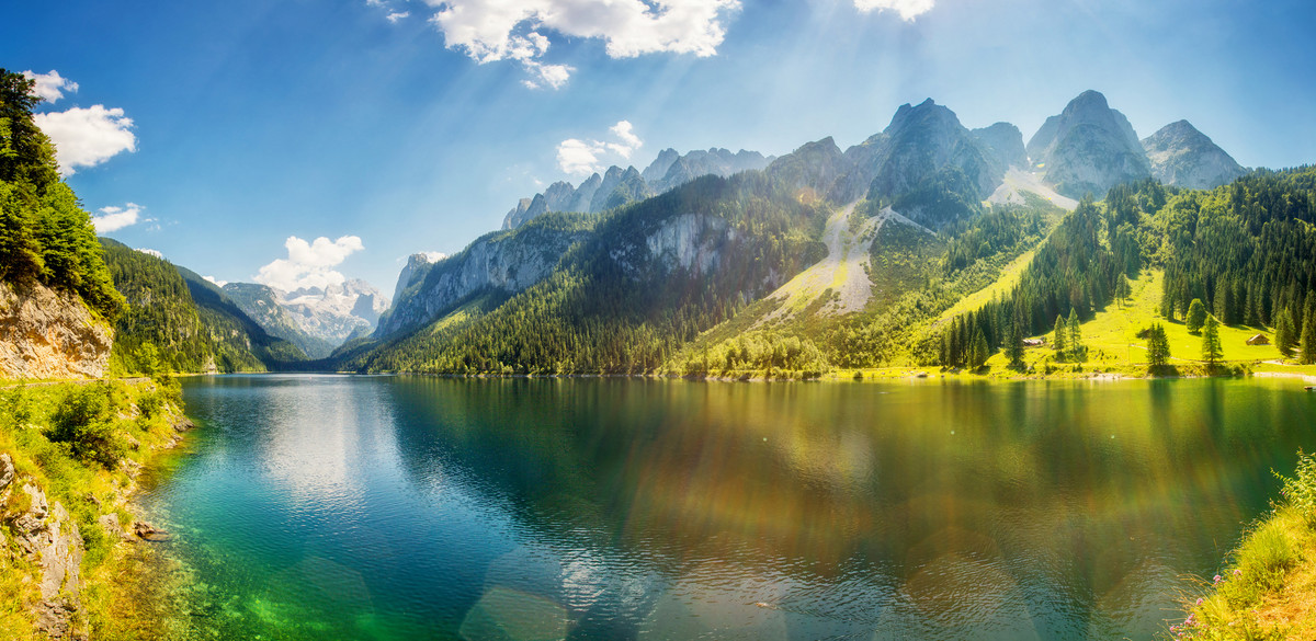 Eine Landschaftsaufnahme eines Bergsees, mit Gebirge dahinter und strahlendem Himmel