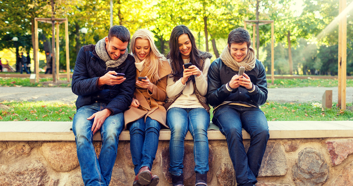 Vier junge Leute sitzen auf einer Mauer und schauen auf ihre Smartphones