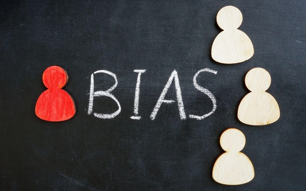 Cognitive biases and their impact on financial decision-making is a core concept in behavioral finance to be explored during your MBA in finance program - A panel with "BIAS" written on it and 4 stylized figures, one of which is red, on the left side, the others on the right side.