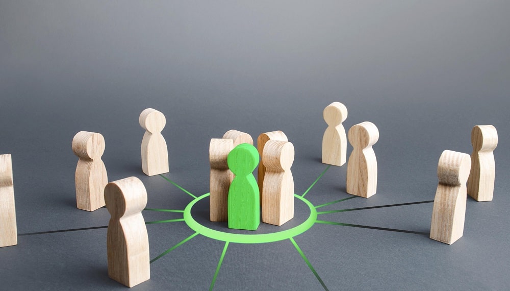 Eine Gruppe von Spielfiguren aus Holz, in der Mitte sticht eine Spielfigur in Grün heraus
